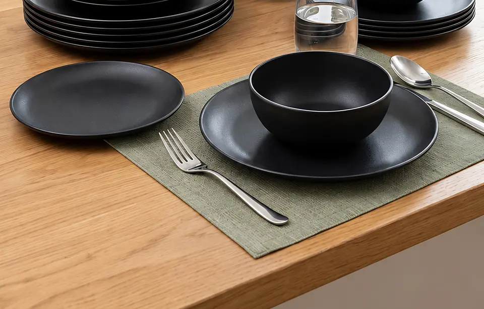 Matte black dinner plate and bowl with a stainless steel fork and spoon on a green placemat