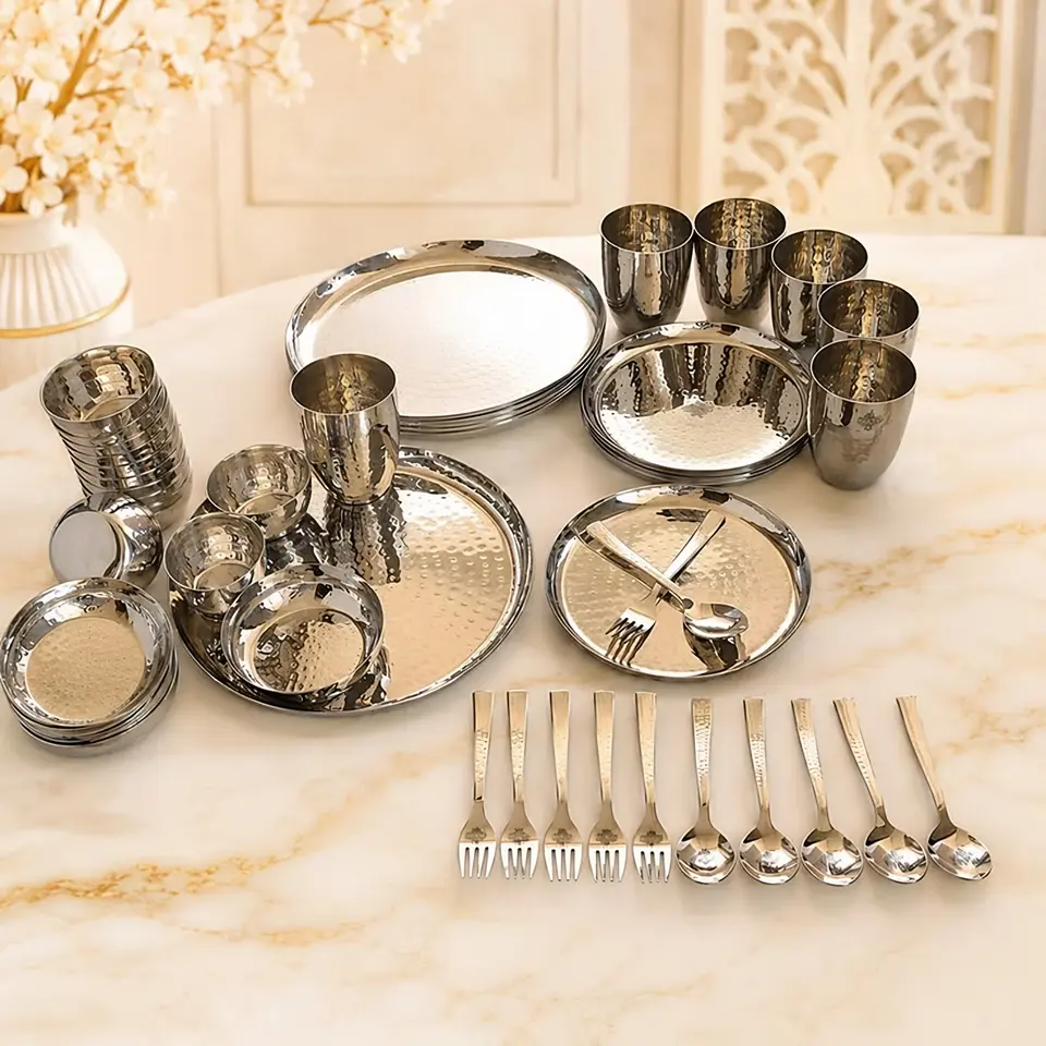 Hammered stainless steel plates, bowls, tumblers, forks and spoons laid out on a marble table